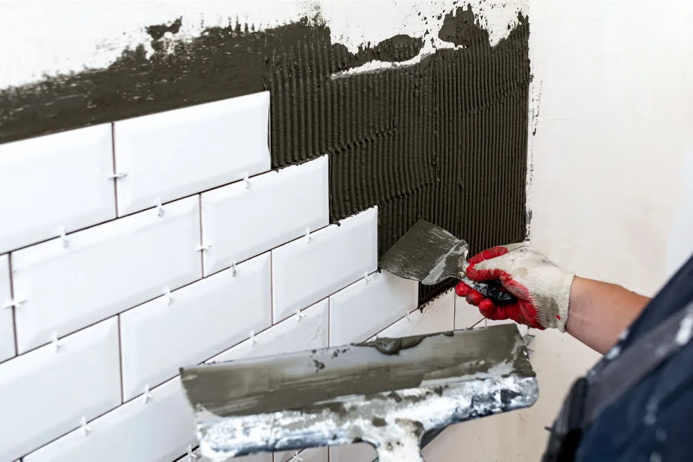 Worker applying black mastic adhesive behind ceramic tiles