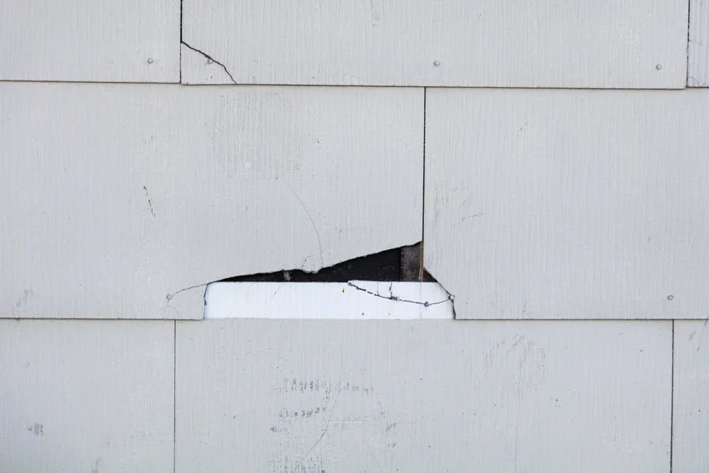 Damaged asbestos siding with visible cracks and a broken shingle showing cracked asbestos siding