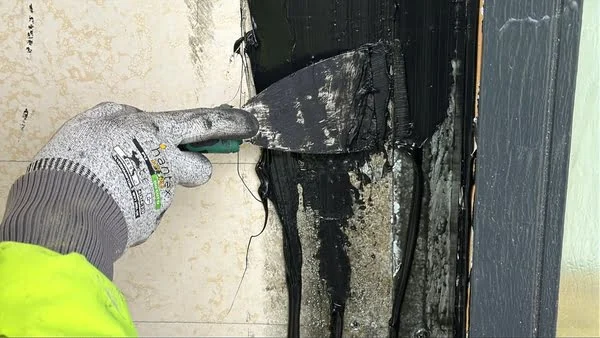 Worker scraping black mastic asbestos adhesive during remediation